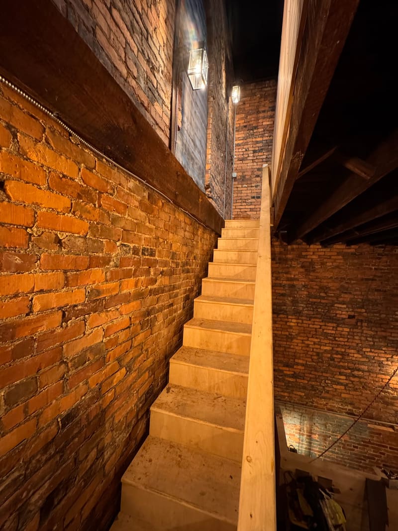 Timber stair rising along the brick tower wall